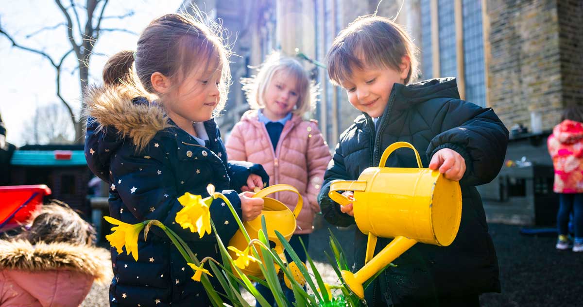Hurlingham School Nursery - three children playing outdoors in playground, with watering cans and daffodils